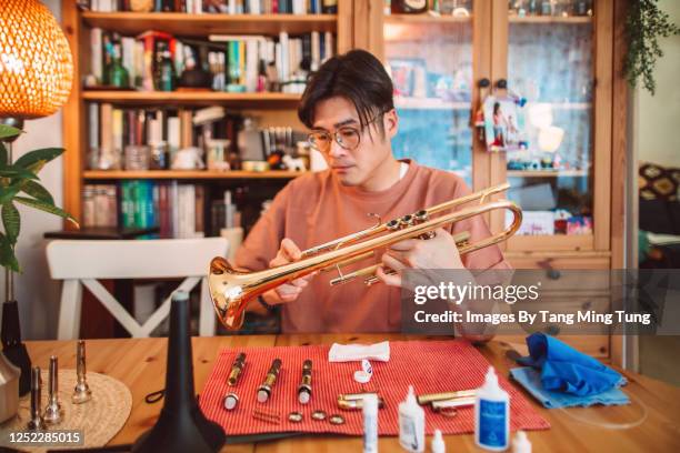 young asian man carrying out maintenace work of his trumpet at home - instrumento de metal fotografías e imágenes de stock