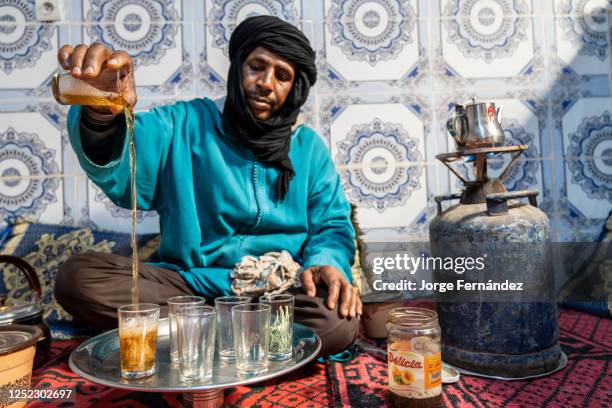 Berber man dressed in djellaba and black turban serving tea in the traditional way.