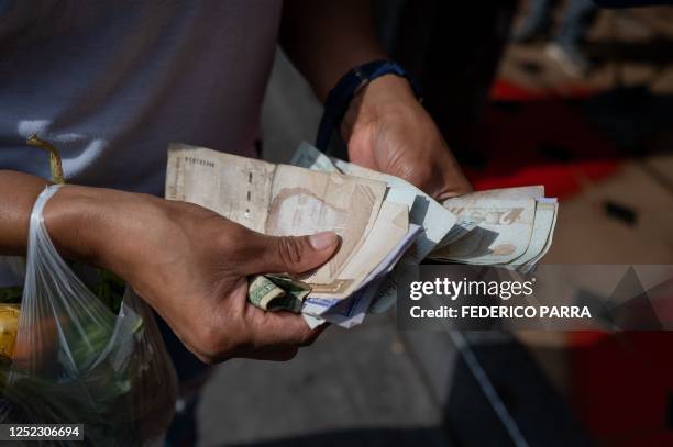 Woman counts Bolivar bills to buy food in the street in Caracas on April 28, 2023.