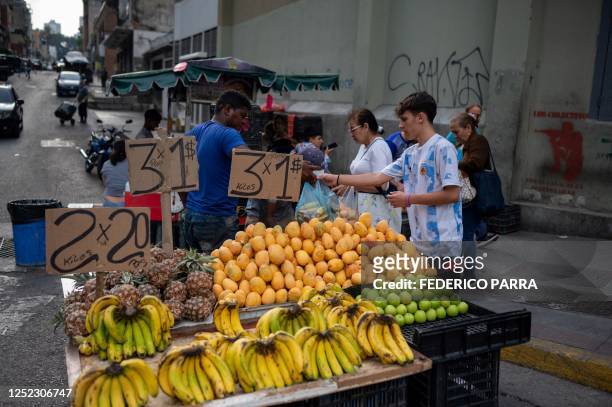 People buy fruit from a street vendor who offer his products in US dollars, in a street of Caracas, on April 28, 2023.