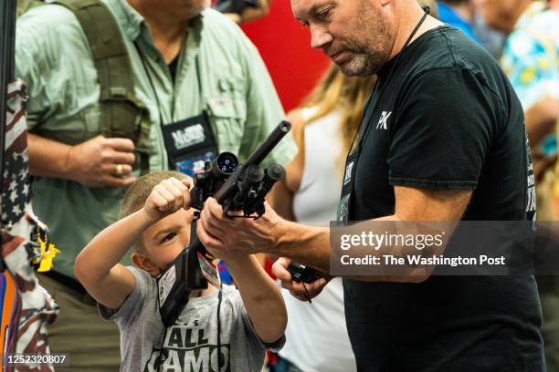 April 15, 2023: An attendee shows a young boy how to hold and load a gun during the National Rifle Association annual convention at the Indiana...