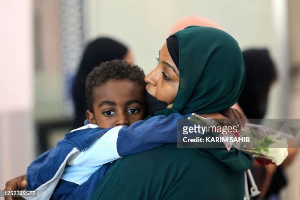Woman carries a child as people fleeing conflict in Sudan arrive at an airport in Abu Dhabi after an evacuation flight, on April 29, 2023. -...