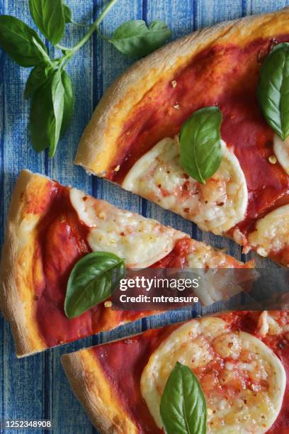 image of sliced, freshly baked homemade margherita pizza, golden buffalo mozzarella cheese circles, rich tomato marinara sauce and fresh basil leaves topping, blue tongue and groove effect background, elevated view - pizza margherita imagens e fotografias de stock