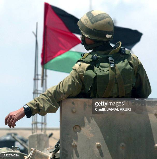 The Palestinian flag flutters as an Israeli soldier sits in the turret of a tank patrolling the streets in the West Bank city of Ramallah 25 June...