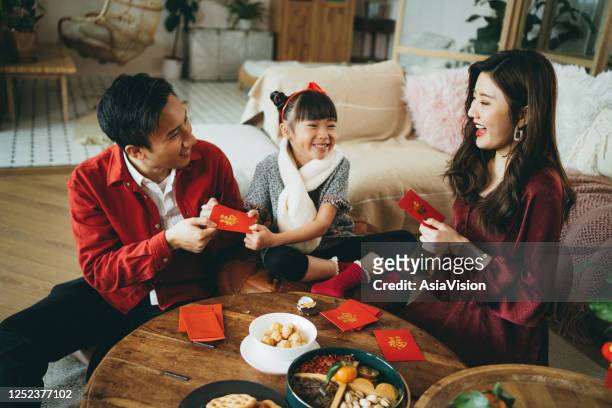 joyful young asian family celebrates chinese new year, parents giving red envelops (lai see) to their daughter and she receives them with both hands - hong kong celebrates chinese new year stock pictures, royalty-free photos & images