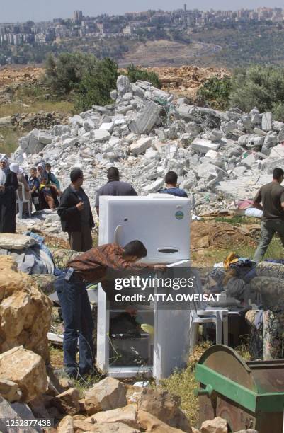 Palestinian man grabs for a bottle of soda from a fridge standing 21 May 2002 near the rubble of his family home, destroyed by the Israeli army the...