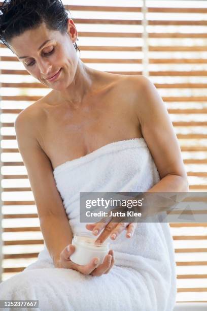 woman in towel applying moisturizer in bathroom - older woman wet hair stock pictures, royalty-free photos & images