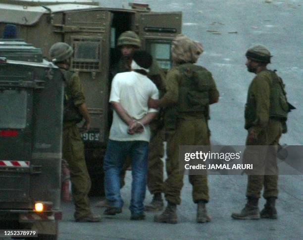 Israeli soldiers escort a blindfolded Palestinian man with his hands tied behind his back, after they arrested him and others just before night fall...