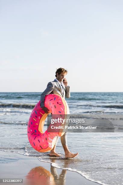 businessman with inflatable donut on sunny ocean beach, los angeles, california - mid adult men fotografías e imágenes de stock