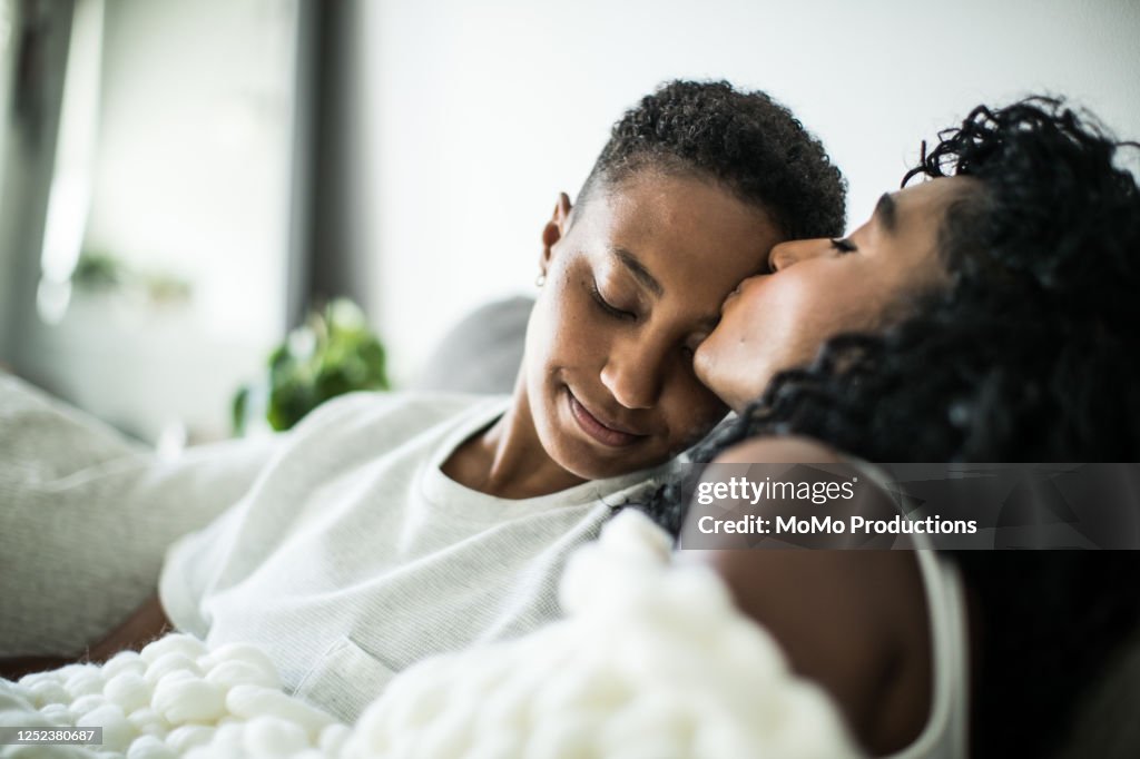 Lesbian couple at home snuggling under blanket