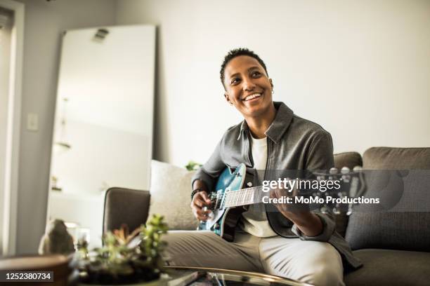 woman playing electric guitar in living room - hipster candid stockfoto's en -beelden