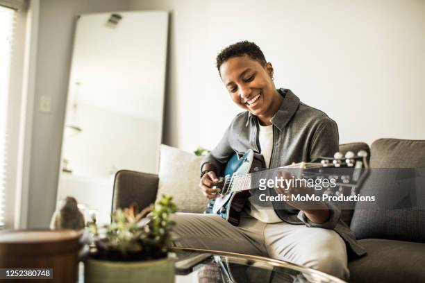 woman playing electric guitar in living room - chitarra foto e immagini stock