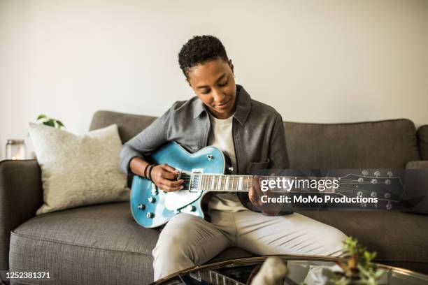 woman playing electric guitar in living room - guitarist stockfoto's en -beelden