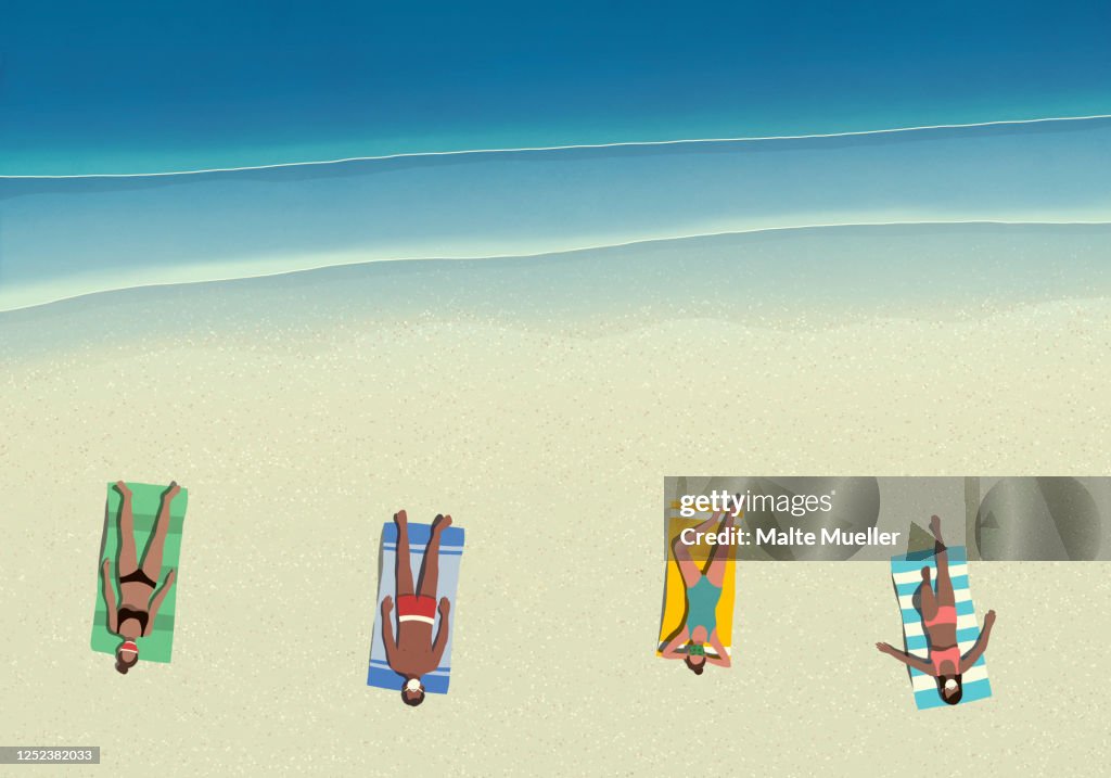 People in protective face masks sunbathing and social distancing on sunny beach