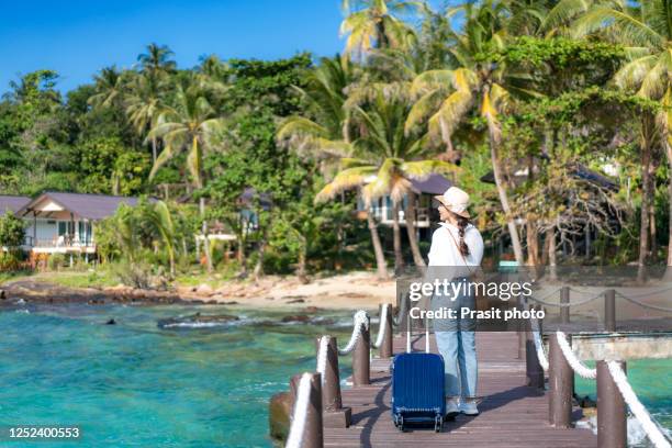 beautiful asian woman with luggage walking in wooden pier in front of summer beach hotel area when she arrive by boat in trat, thailand. travel, summer holidays and vacation concept. - junge frau allein stock-fotos und bilder