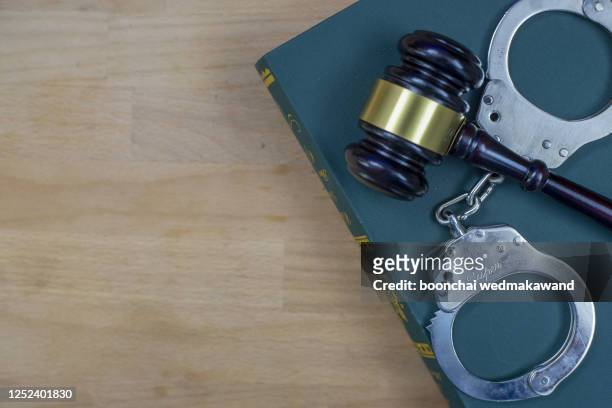 gavel and handcuffs on the law book over the wooden table background - lady justice fotografías e imágenes de stock