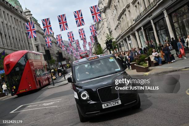 Black cab and a red London bus passes beneath Union flags in central London, on April 30, 2023 ahead of the coronation ceremony of Charles III and...