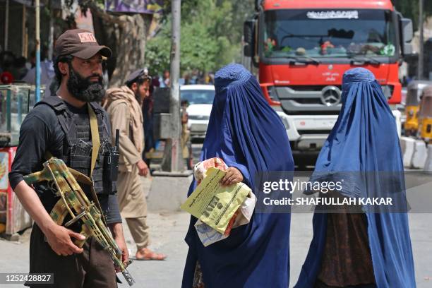 Afghan burqa-clad women walk past a Taliban security personnel along a street in Jalalabad on April 30, 2023.