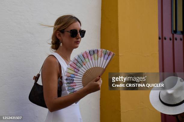 Spectator cools off with a fan as she arrives for the Feria de Abril bullfighting festival at La Maestranza bullring in Seville on April 30, 2023.
