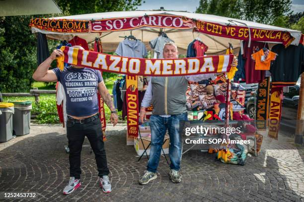 Men from 'Bancarella Roma', who sells gadgets for AS Roma fans displays a large yellow and red scarf with the words 'Lazio Merda' written on it....