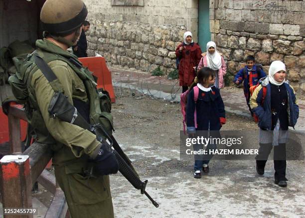 Palestinian children pass in front of a check point in the divided West Bank city of Hebron 08 February 2003.The Middle East peace process received a...