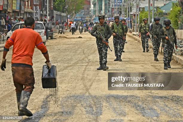 Labourer sprays asphalt at a road contruction site as Indian paramilitary troopers patrol along a street in Srinagar on May 1, 2023.