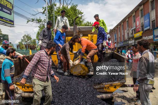 Kashmiri labourers work stand on a road paver to lay asphalt concrete on a road in the city center during the International Labor Day on May 01, 2023...