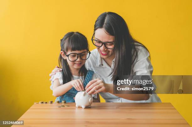 little asian cute girl putting money to piggy bank with her mother - silver putter stock pictures, royalty-free photos & images