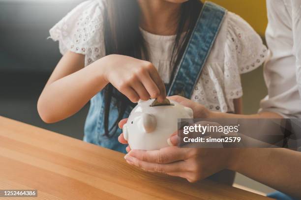 little asian cute girl putting money to piggy bank with her mother - family savings stock pictures, royalty-free photos & images