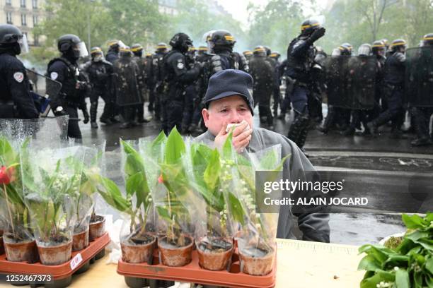 Street vendor selling traditional sprigs of lily of the valley reacts to teargas as French Republican Security Corps police officers take positions...