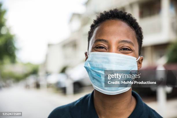 young woman wearing surgical mask in front of home - griepmasker stockfoto's en -beelden