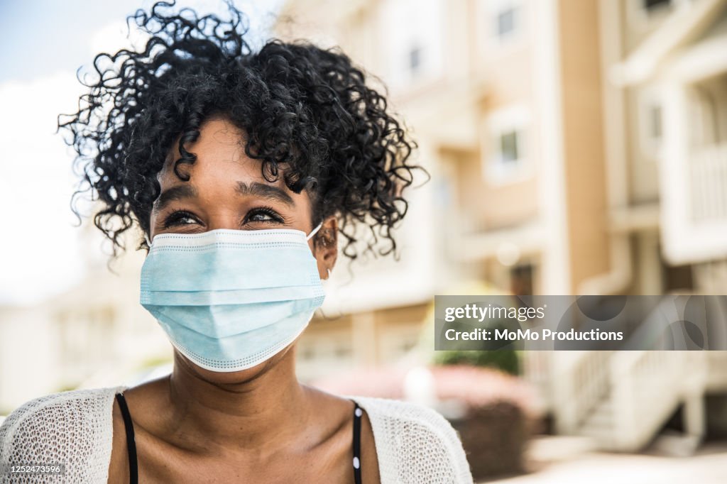Young woman wearing surgical mask in front of home
