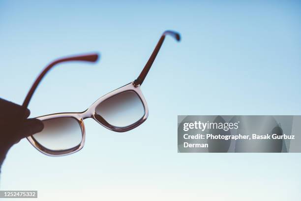 a woman's hand holding sunglasses blue sky on the background - eyeglass frames stock pictures, royalty-free photos & images