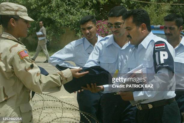 Soldier distributes uniform pants to Iraqi policemen in their new police garb, in which the Arabic phrase 'God is Great', or 'Allahu Akbar', was...