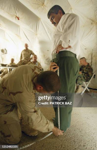 Jonathan Stone from the US Military Police measures the pants leg of an Iraqi man 28 May 2003 in Baghdad before he is given a new Iraqi police...