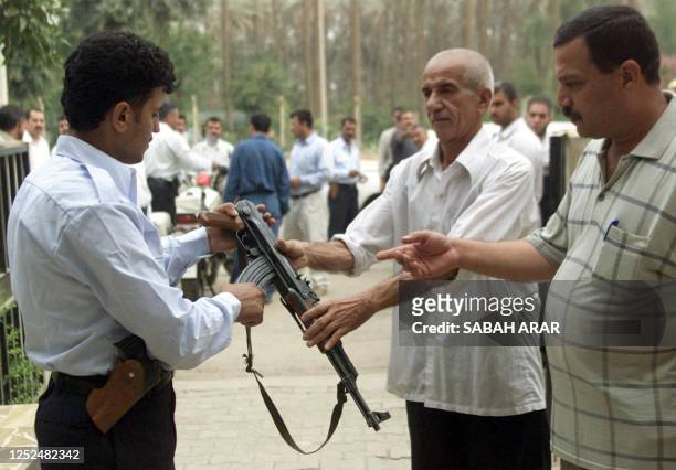 Iraqi civilians hand over a Kalashnikov automatic rifle at a police station in Baghdad, 02 June 2003, complying to the US-led administration...