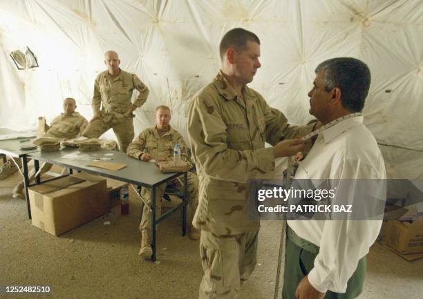 Jonathan Stone from the US Military Police measures the collar of an Iraqi man 28 May 2003 in Baghdad before he is given a new Iraqi police uniform...