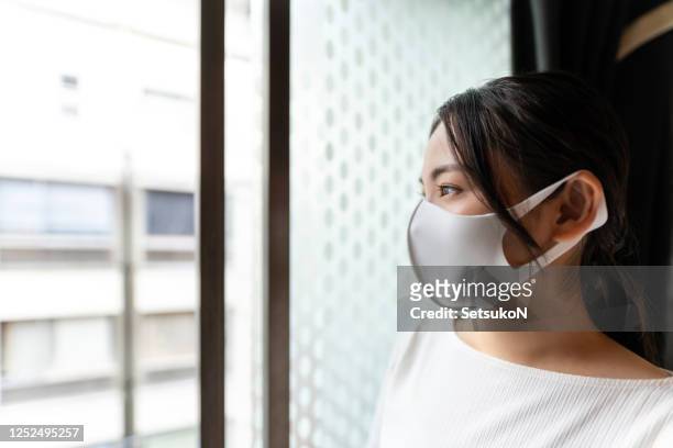 asian woman with mask standing by the window - state of emergency stock pictures, royalty-free photos & images