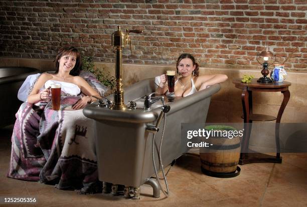 Two unidentified girls relax, one taking a beer bath, both drinking a pint of Czech beer, 17 March 2006 in Chodova Plana near Marianske Lazne in a...