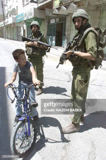 Palestinian boy on his bicycle rides by Israeli soldiers, 30 August 2003, during curfew in the divided West Bank city of Hebron. At least two...