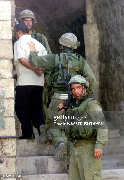 An Israeli soldier leans his hand on the back of a handcuffed unidentified Palestinian resident as he is made to enter before the soldiers inside a...