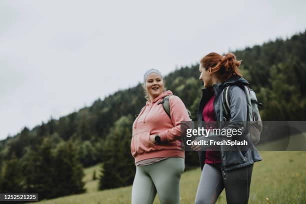 dos felices mujeres jóvenes con mochilas pasar el día en la naturaleza juntos - voluptuous woman fotografías e imágenes de stock
