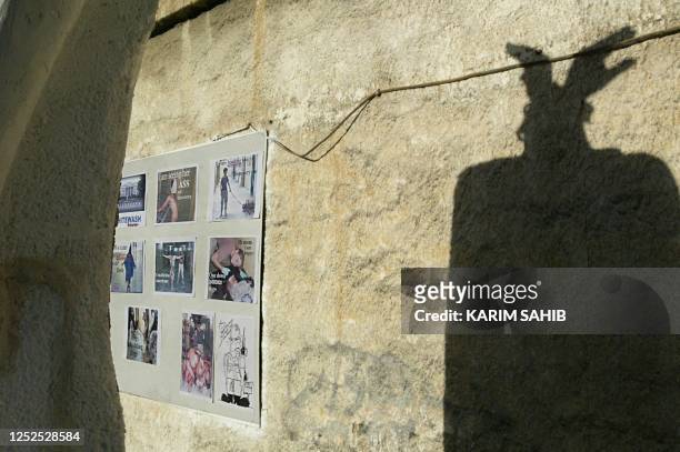 The shadow of chained wrists representing the head of the "statue of Liberty" are reflected on a wall close to pictures of Iraqi prisoners stripped...