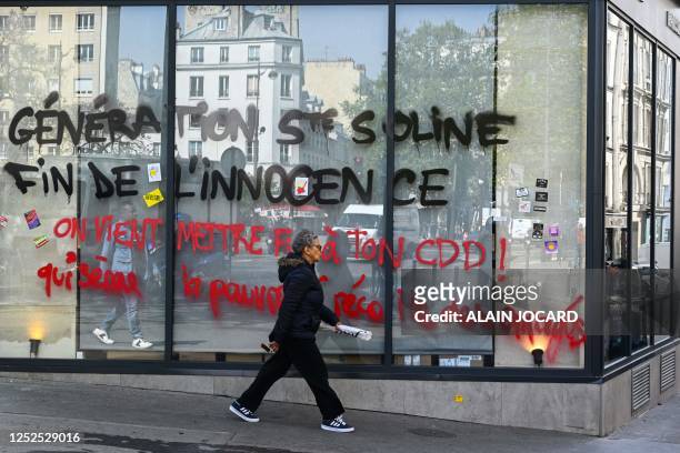 Woman walks past a bakery-pastry store displaying a graffiti on its windows reading "Generation Sainte-Soline, end of innocence, We have just ended...