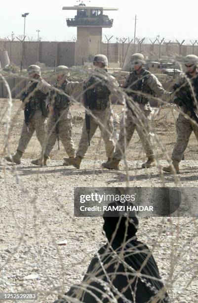 Soldiers walk past an Iraqi Muslim woman sitting on the ground near concertina wire during a protest against the mistreatment of prisoners and...