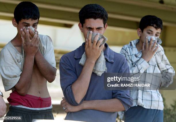 Three Iraqi youths cover their face because of the stench of a charred car hit by a roadside bomb 24 May 2004 in Baghdad's Zayun neighborhood. Three...