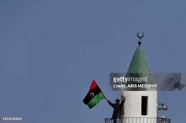 Libyan rebel waves the Kingdom of Libya flag in the town of Bin Jawad on March 27, 2011 as rebels pushed westwards in hot pursuit of Moamer Kadhafi's...