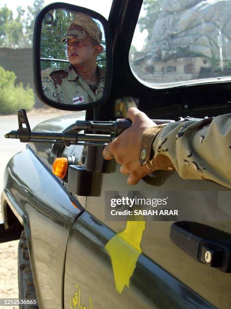An Iraqi National Guardsman is seen through the side view mirror of a car as he patrols northern Baghdad 07 July 2004. US and Iraqi armed forces have...