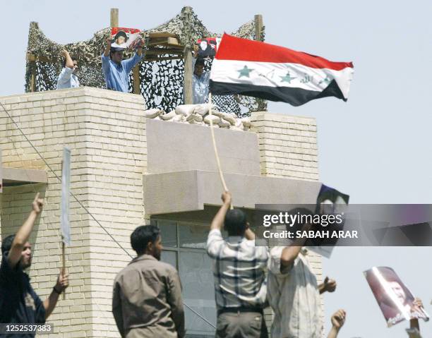 Iraqi policemen hold up pictures of radical Iraqi Shiite Muslim cleric Moqtada Sadr as they stand guard atop a police station near the so-called...