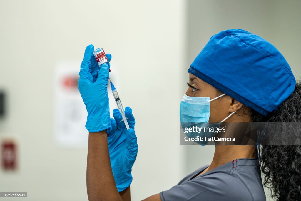 Female Medical Professional drawing Covid-19 vaccine from vial with a syringe
